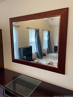 Front view of rectangular wall mirror showing wooden frame and reflective surface. Room and furniture reflected in mirror.