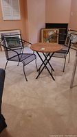 Full view of round wicker-topped metal folding table and two black metal mesh chairs.