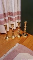 Four brass candle sticks displayed against curtain and floor background with two pairs of different base shapes.