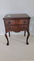 Front view of the antique wooden cutlery chest showing two drawers with tarnished metal handles and the carved legs with claw feet.