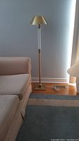 Full view of brass floor lamp standing by a sofa and carpet showing overall condition and size.