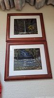 Full view of two framed prints stacked vertically on a textured wall showing tropical scenes