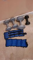 Photo showing two 5 lb gray dumbbells, one 10 lb black dumbbell, and two blue ankle weights.