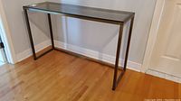 Front side view of metal and glass hall table against wall on hardwood floor.