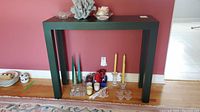 Front view of the narrow black hall or display table with various candles and decorative items on floor beneath it.
