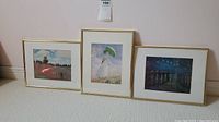 Full view of the three impressionist prints framed and resting against a wall on carpet.