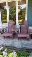Two reddish wooden Muskoka chairs on a stone patio in front of a window, showing front view.
