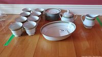 Full set arranged on table showing eight cups with matching saucers, sugar bowl, creamer, and oval serving bowl.