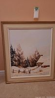 Full view of the framed and matted rural winter scene painting showing snow-covered trees, fence, and rustic building.
