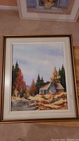 Full view of the framed oil painting showing the entire rural landscape with house, river, and trees.