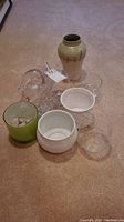 View of all ceramic pots, glass vases, and glass flower frog arranged on carpeted floor showing lot contents.