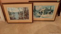 Two framed prints by Keirstead, one showing Kawartha Lakes and birch trees, and one showing rustic cabin in snowy woods.