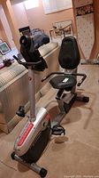 Recumbent bike angled sideways showing seat, pedals, and console area in a basement room