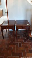 Two wooden side tables with one drawer each, both placed side by side on a tiled floor.
