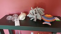 Lot overview showing all items: glass sea urchins, faux coral, glass conch shell, and fish plate on black shelf against pink background.