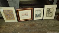 Four framed art prints side by side on wooden floor showing size and framing styles