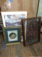 Photo showing three framed artworks including WQED Auction print, doll artwork, and framed classical green-mat print