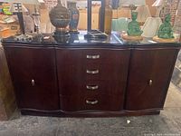 Front view of Bernhardt vintage serpentine front wood buffet with items displayed on top (not included). Shows drawer and cabinet configuration, metallic pulls, and black stone top.