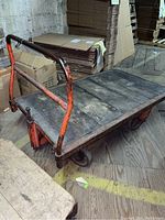 Photo of the side and top of the metal platform cart showing wooden base and orange metal frame with wear.