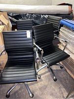 Four black adjustable office armchairs with ribbed seats and backs, chrome armrests, and star swivel bases with casters.