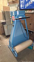Front left view of blue Padpak Jr cushioning system, showing paper roll dispenser and control box with labels and warnings.