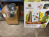 Boxed mini tabletop water fountains visible beside boxed Treehaus adjustable artist easel