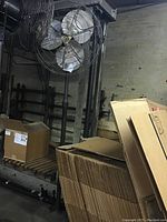 Full view of the tall industrial fan showing the metal blades, cage, support pole, and base.