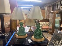 Pair of green ceramic lamps with Asian themed figurines, pleated lampshades on table in warehouse setting