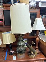 Four lamps displayed including three table lamps with fabric shades and one brass desk lamp.