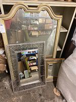 Photo showing three mirrors grouped together: a large wood framed mirror with a curved top behind two smaller mirrors, one metal framed with bead details and one gilt carved frame mirror.
