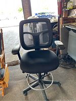 Front view of black office chair showing mesh backrest, padded seat, armrests, and wheel base.