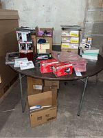 Wide shot of round table with assorted office supplies including staplers, plastic document wallets, clipboards, index cards, boxes, and punchers.