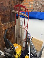 Full view of the Flexible Flyer III sled showing wooden slats and red metal frame, leaning against a wooden wall with surrounding items.