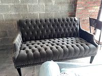Full view of the dark gray velour tufted sofa with nailhead detailing and tapered dark wooden legs, showing front and seating area.