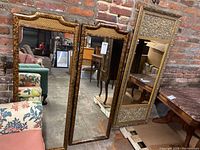 Two Asian inspired wall mirrors standing against a brick wall, showing size difference and style of frames.