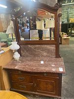 Full front view of vintage wood washstand showing stone top, storage cabinet, and beveled mirror on wooden frame.