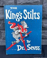 Front cover of The King's Stilts children's book showing blue cover with white title text and illustration of character on red stilts.