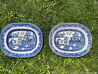 Photo of paired Blue Willow platters side by side on grass, showing similar size and pattern with minor damage.
