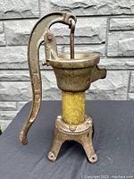 Front angle of the antique brass and cast iron water pump on black cloth against stone wall.