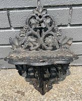 Front view of antique cast iron wall shelf showing ornate floral and scroll details and textured shelf surface.
