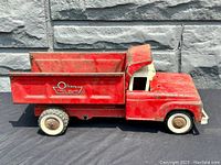 Left side profile of the red and white pressed steel dump truck with unopened dump bed showing the Olsen Truck Bodies logo on the side.