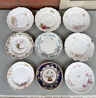 Top view of nine decorative antique plates arranged in a 3x3 grid on a grey surface