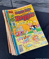 Top view of the comic stack showing the cover of a Richie Rich and Mean Cousin Reggie comic featuring colorful illustration of characters in a pie fight.