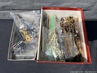 Overview of assorted clock hands in plastic bags and a shoebox container