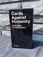 Front view of black box with white text for Cards Against Humanity party game, CA edition