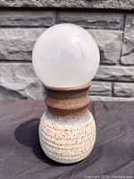 Front view of mid century modern pottery table lamp with white glass globe and speckled ceramic base.