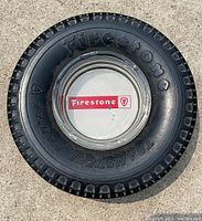 Top-down photo of the miniature Firestone tire ashtray showing clear glass ashtray with red and white Firestone decal in center and tire details around sidewall.