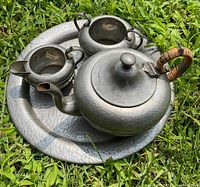 All items of the vintage hammered pewter tea set seen from above on grass.