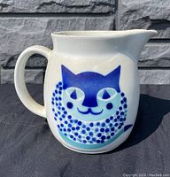 Side view of porcelain pitcher showing full blue cat design, handle and spout.