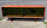 Front view of teak sideboard with both smoked glass sliding doors closed, showing wood grain top and base.